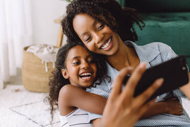 Junge Frau mit ihrer kleinen Schwester, die zu Hause ein Selfie mit ihrem Mobiltelefon macht. - JLPSF04594