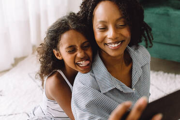 Fröhliche afrikanische Frau mit süßem Mädchen, das die Zunge herausstreckt, macht ein Selfie zu Hause. Mutter und Tochter machen ein Selfie. - JLPSF04595