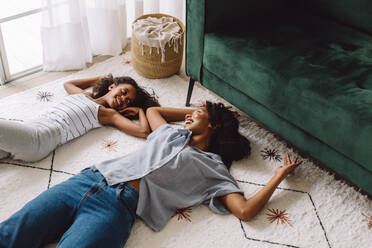 Afrikanische Frau mit Mädchen auf Teppich liegend, Mutter und Tochter schauen sich an und lächeln. - JLPSF04597