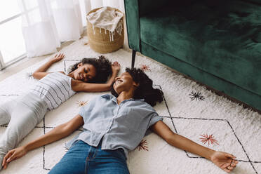 Mutter und Tochter tun so, als würden sie auf dem Boden schlafen. Afrikanische Frau mit Mädchen entspannt sich auf dem Wohnzimmerteppich. - JLPSF04598