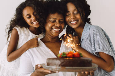 Woman holding her birthday cake with sparklers and her daughters. Girls with mother celebrating birthday. - JLPSF04644