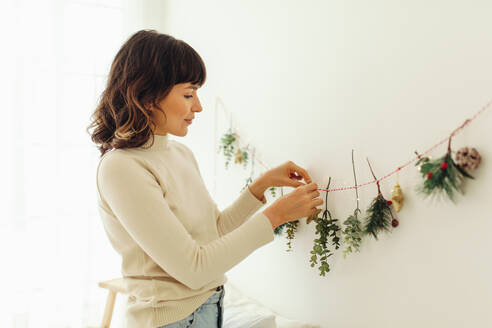 Woman decorating home for christmas. Woman tying twigs to a lace and decorating wall. - JLPSF04671