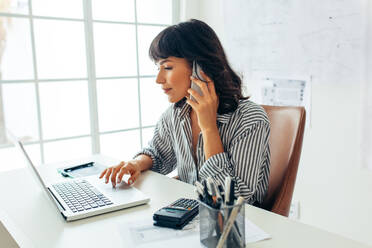 Unternehmerin, die ein Unternehmen leitet und über ein Mobiltelefon spricht. Geschäftsfrau, die an ihrem Schreibtisch sitzt und an einem Laptop arbeitet. - JLPSF04696