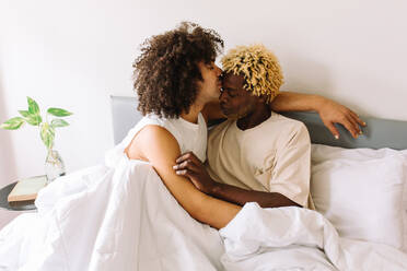 Ethnic gay couple embracing each other with their eyes closed. Two young male lovers touching their faces together while lying in bed in the morning. Affectionate young gay couple bonding at home. - JLPSF04751