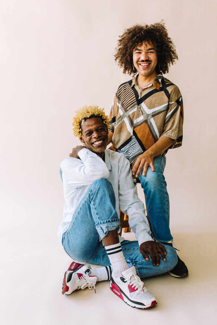 Cheerful young gay couple smiling at the camera. Two young male lovers  sitting confidently against a studio background. Young gay couple posing  together in a studio. stock photo