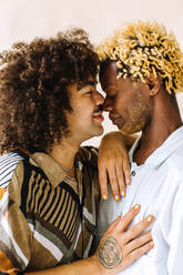 Zärtliches junges schwules Paar, das sich in einem Studio an der Nase fasst. Zwei junge männliche Liebhaber, die mit geschlossenen Augen vor einem Studiohintergrund posieren. Junges schwules Paar in romantischer Stimmung. - JLPSF04789