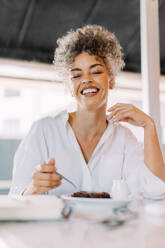 Carefree mature woman having some cake in a cafe. Happy mature woman smiling at the camera while sitting at a cafe table. Mature woman having lunch alone. - JLPSF04843