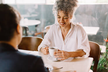 Businesswoman meeting with a client in a cafe. Happy mature businesswoman smiling while having a discussion with her business partner. Woman holding a cup of coffee during a meeting. - JLPSF04848