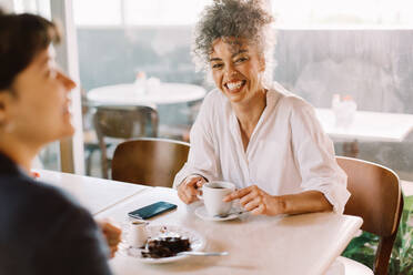 Fröhliche Geschäftsfrau, die mit ihrem Partner in einem Café Kaffee trinkt. Glückliche reife Geschäftsfrau, die lächelt, während sie ein Gespräch mit einem Kunden führt. Geschäftsfrau, die ein Treffen in einem Café hat. - JLPSF04849