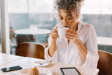 Reife Unternehmerin, die in einem Café an einer Tasse Kaffee nippt. Reife Geschäftsfrau, die in der Mittagspause allein in einem Café sitzt und Kaffee trinkt. - JLPSF04854