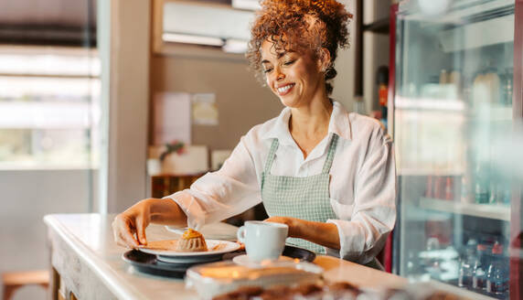 Cheerful female barista serving an order in a cafe. Mature cafe owner putting an order on a serving tray while standing behind the counter. Successful business owner working alone. - JLPSF04889