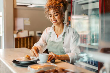 Reife Barista-Frau, die eine Bestellung in einem Café serviert. Reife Café-Besitzerin, die eine Bestellung auf ein Serviertablett legt, während sie hinter dem Tresen steht. Erfolgreiche Geschäftsinhaberin, die allein arbeitet. - JLPSF04890