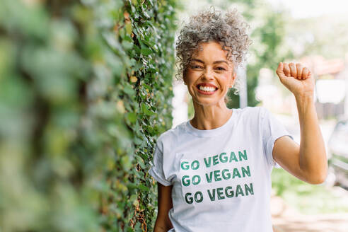 Fröhlich lächelnde Veganer-Aktivistin, die alleine im Freien steht. Fröhliche reife Frau, die sich für Veganismus einsetzt und ein T-Shirt mit der Aufschrift 