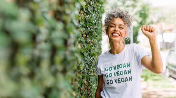 Unbekümmerte reife Veganer-Aktivistin, die fröhlich lächelt, während sie alleine im Freien steht. Glückliche reife Frau, die sich für Veganismus einsetzt, während sie ein T-Shirt mit der Aufschrift 