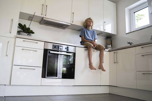 Boy sitting on kitchen counter at home - NJAF00025