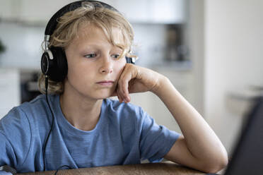 Boy with wired headphones leaning on elbow at table - NJAF00029