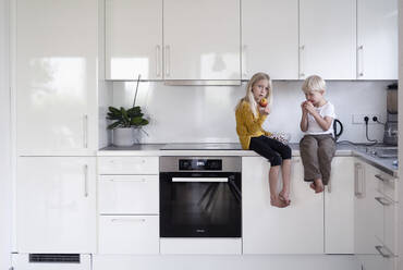 Junge und Mädchen mit Äpfeln auf der Küchentheke zu Hause - NJAF00030