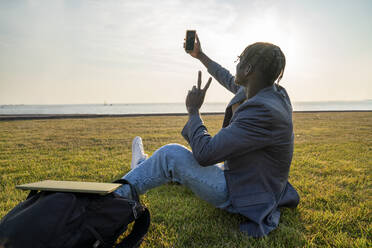 Junger Geschäftsmann, der ein Selfie mit seinem Smartphone macht, während er im Gras sitzt - VPIF07511