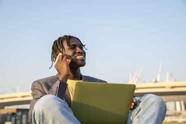 Happy businessman talking on mobile phone sitting with laptop - VPIF07514