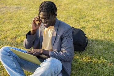 Happy businessman using laptop and talking on mobile phone - VPIF07517