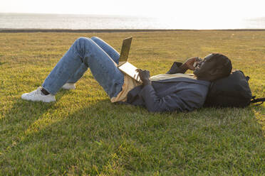 Smiling young businessman using laptop and talking on mobile phone - VPIF07518