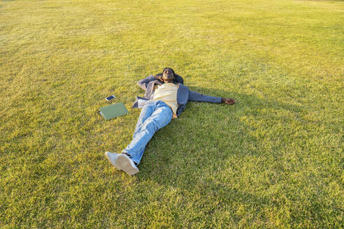 Businessman with mobile phone and laptop resting on grass - VPIF07521