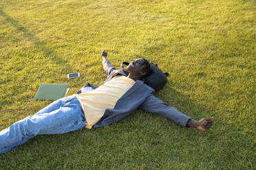 Smiling businessman with mobile phone and laptop relaxing on grass - VPIF07522