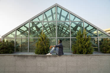 Businessman in front of glass house at sunset - VPIF07532