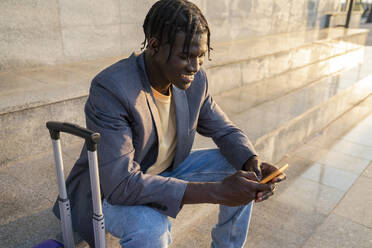 Lächelnder Geschäftsmann, der auf einer Treppe sitzend ein Smartphone benutzt - VPIF07545