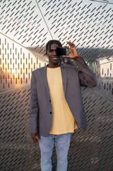 Smiling businessman covering eye with dark glass in front of metal wall - VPIF07606