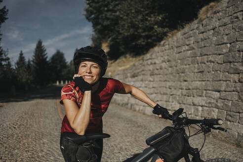 Smiling woman wearing helmet leaning on bicycle seat - DMGF00860