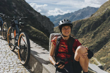 Woman sitting on wall by bicycle - DMGF00867