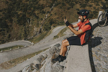 Cyclist photographing through smart phone sitting on wall at Gotthard Pass - DMGF00870