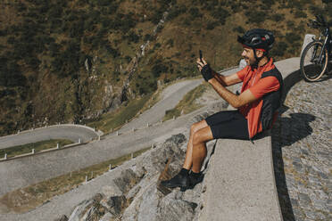 Radfahrer fotografiert mit seinem Smartphone auf einer Mauer am Gotthardpass - DMGF00870