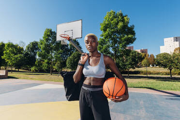 Selbstbewusster Basketballspieler mit Sportball auf dem Platz an einem sonnigen Tag - MEUF08176