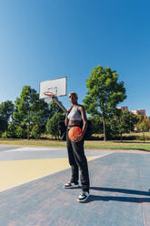 Junge Sportlerin mit Basketball im Hof an einem sonnigen Tag - MEUF08177