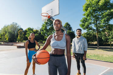 Confident friends with ball in basketball court on sunny day - MEUF08179