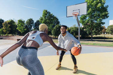 Lächelnder Sportler spielt Basketball mit einem Freund auf einem Sportplatz - MEUF08181