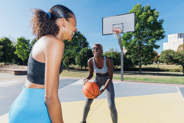 Glückliche Sportlerinnen spielen Basketball auf dem Platz an einem sonnigen Tag - MEUF08182