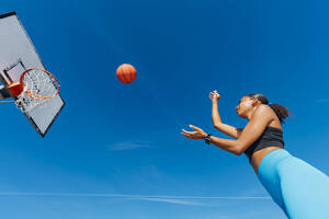 Sportlerin, die an einem sonnigen Tag einen Basketball in einen Korb wirft - MEUF08190