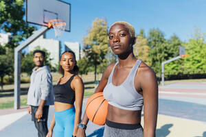 Selbstbewusste Sportlerin mit Basketball von Freunden im Gericht - MEUF08197