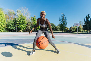 Junge Sportlerin dribbelt Basketball auf dem Sportplatz - MEUF08202