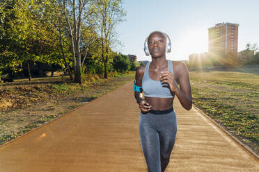 Young athlete jogging and listening to music through headphones in park - MEUF08256