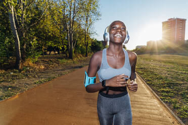 Happy sportswoman listening to music on headphones and jogging in park - MEUF08257