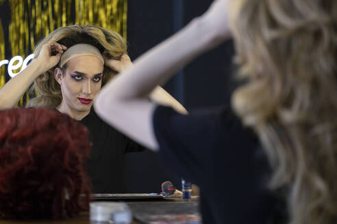 Junge Dragqueen mit Perücke betrachtet den Spiegel in der Umkleidekabine - JBUF00007