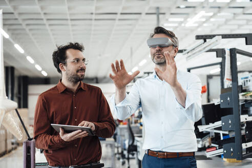 Geschäftsmann mit einem Kollegen, der einen Virtual-Reality-Simulator trägt und in der Industrie gestikuliert - JOSEF13792