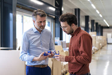 Mature businessman with colleague examining machine part at warehouse - JOSEF13808