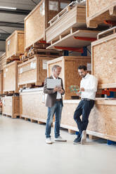 Businessman holding laptop talking to colleague standing in warehouse - JOSEF13838