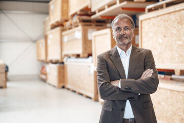 Senior businessman with arms crossed standing at warehouse - JOSEF13839