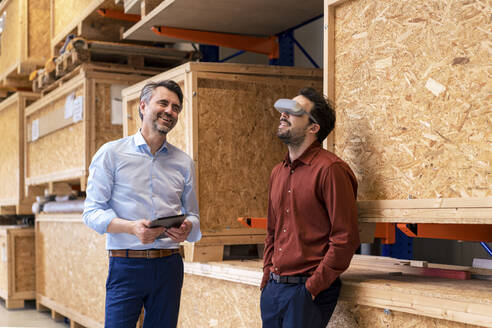 Glücklicher Geschäftsmann mit einem Kollegen, der einen Virtual-Reality-Simulator trägt - JOSEF13844